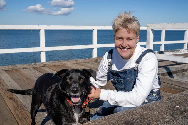 Lizanne smiling on a pier by the water with Butler, a black dog