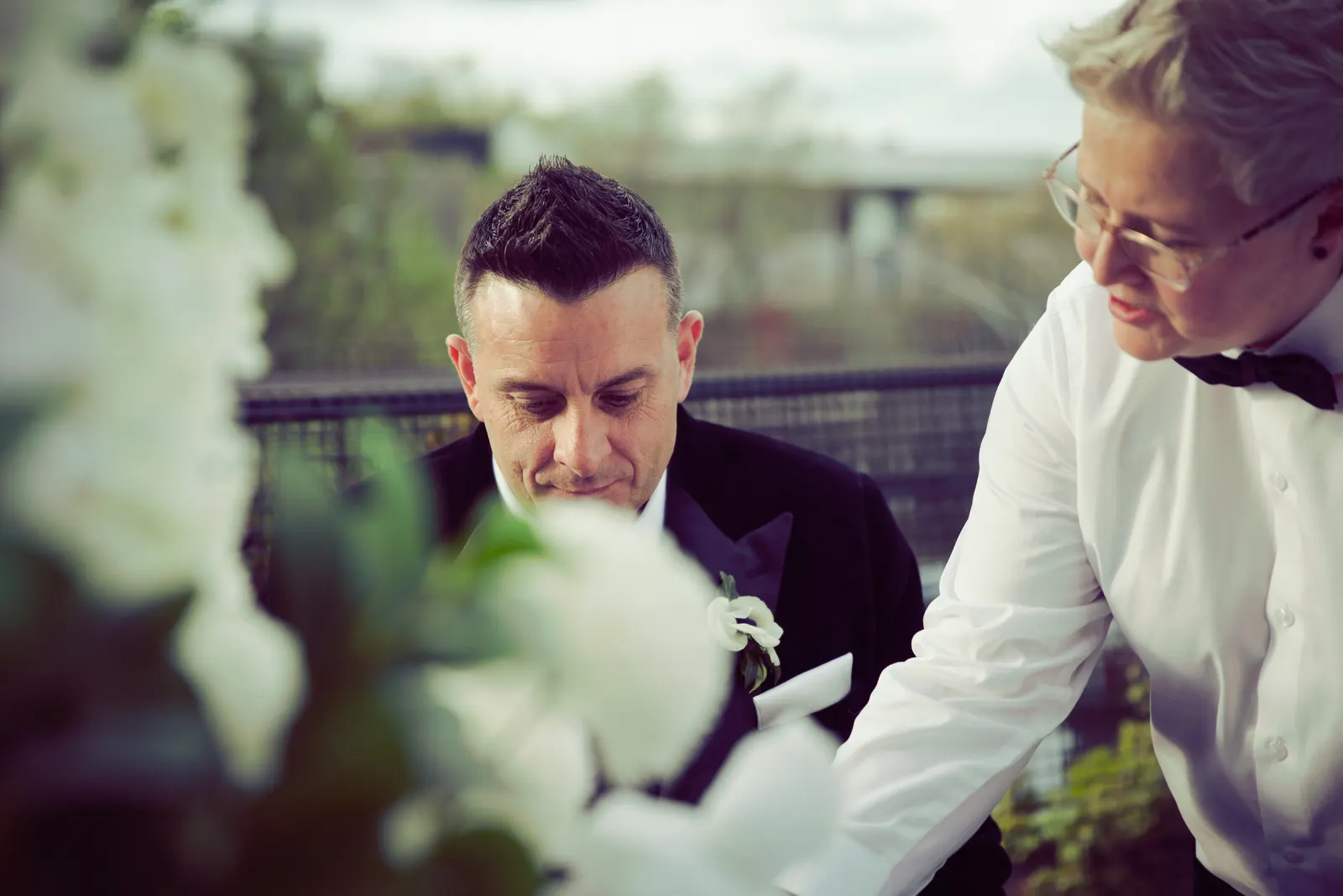 Lizanne leaning in to help a groom with his vows, surrounded by white flowers