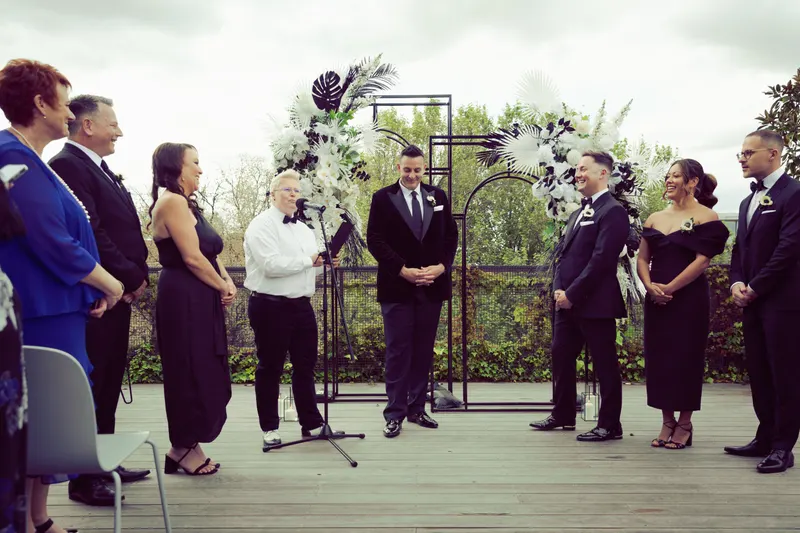 Wide view of an outdoor wedding ceremony in front of a dark metal arch of white flowers