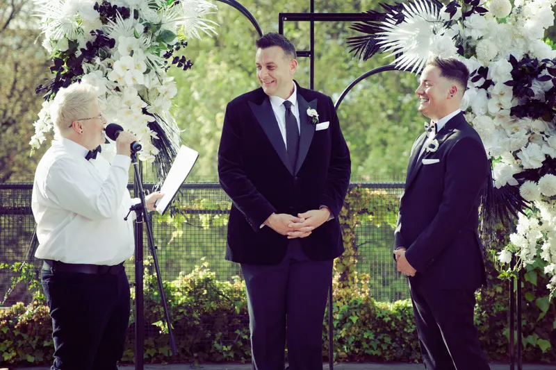 Lizanne officiating between two grooms under a floral arch