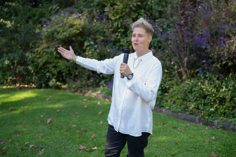 Lizanne gesturing warmly while emceeing outdoors with a microphone