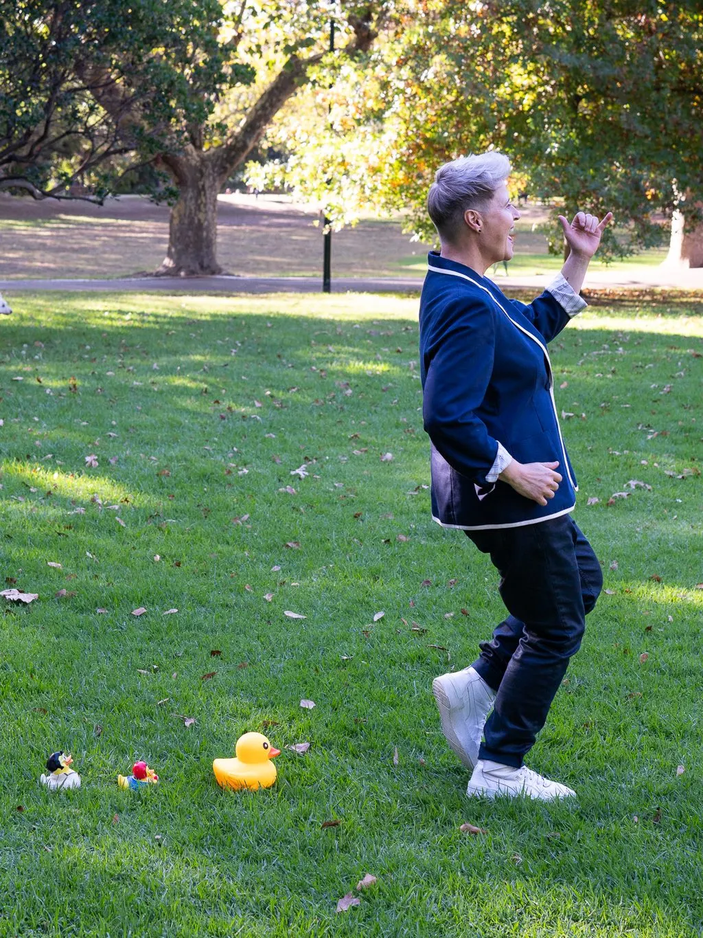 Lizanne dancing on the grass in a navy blazer, next to three rubber ducks